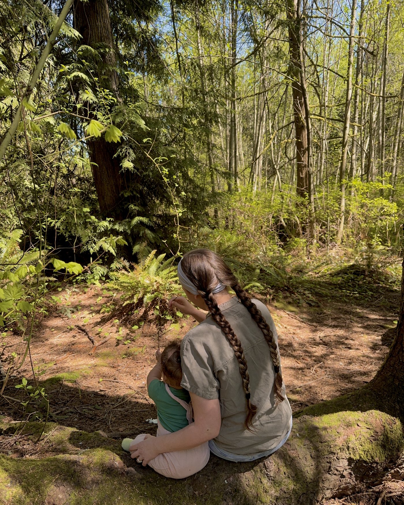 Mattison and her daughter sitting on a mossy log, exploring a fern in the forest
