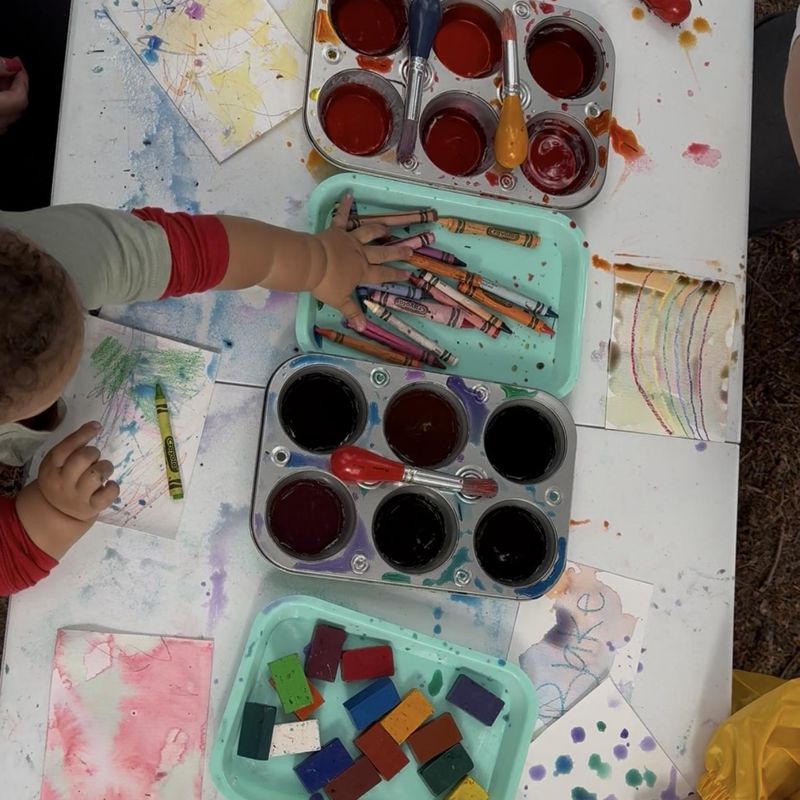 Toddlers drawing with crayons and painting watercolor over the top at an art table