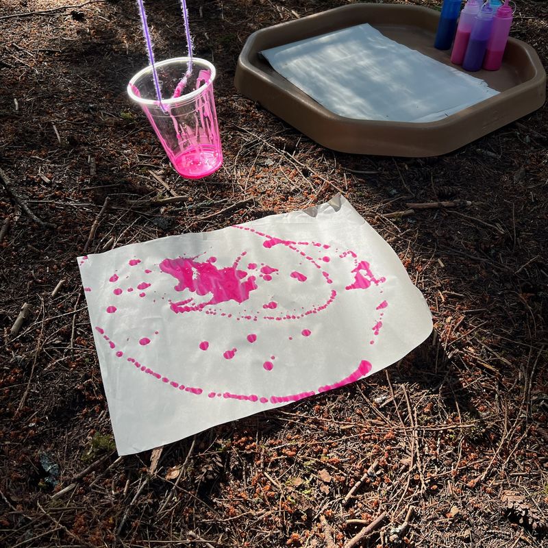 A paint pendulum cup hanging over paper covered in pink paint drips