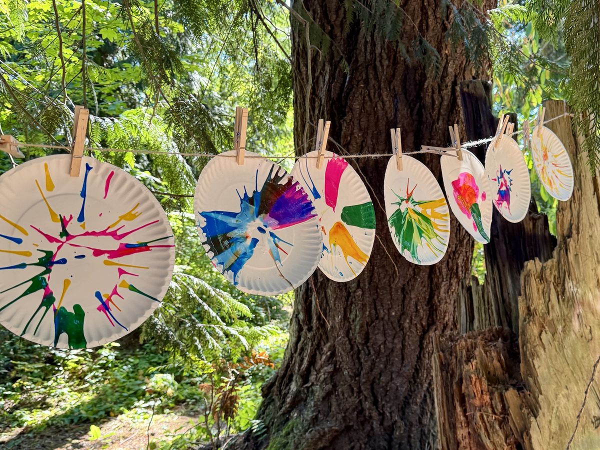 Colorful spin art paper plates drying on a clothesline between forest trees