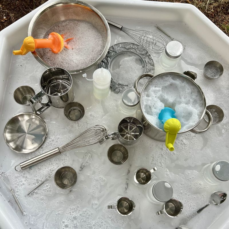 A tray of bubble soup with pots, whisks, sifters, and cups in soapy water