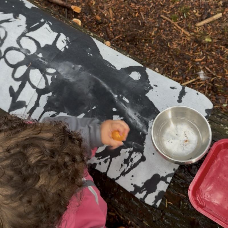 A toddler painting with water on a magic water canvas laid across a fallen log