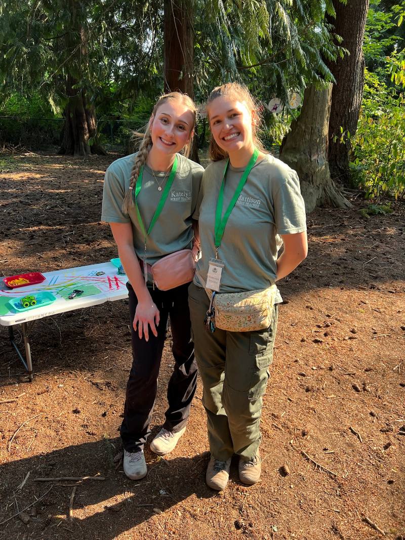 Katelyn and Mattison smiling side by side in matching Forest Teacher shirts at a Little Roots class