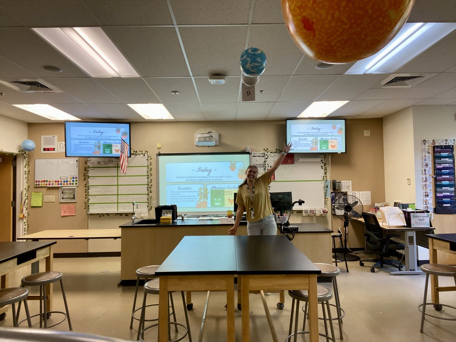 Mattison smiling with one arm raised at the front of her middle school science classroom